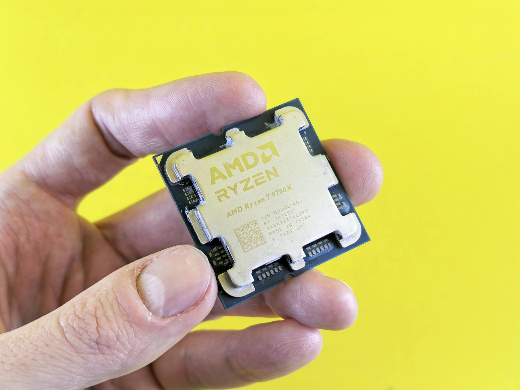 Detailed shot of AMD Ryzen 7 9700X processor held against bright yellow background.