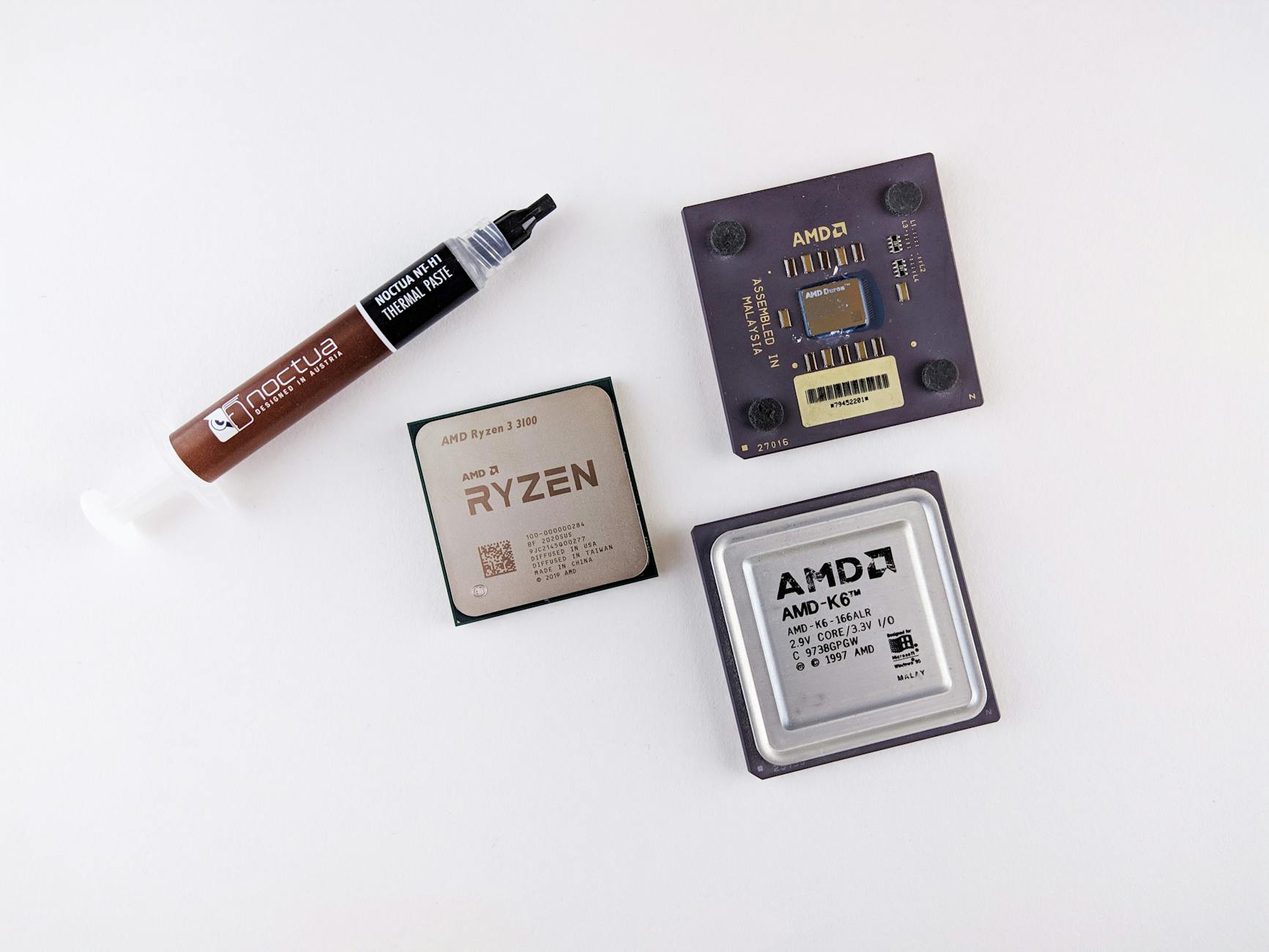 High-angle view of AMD processors and Noctua thermal paste on a white surface.